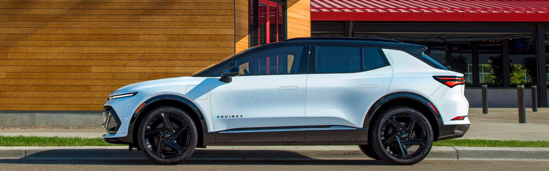 2025 Chevrolet Equinox EV in light blue shown in a full side profile, featuring a black roof, sleek aerodynamic design, large alloy wheels, and modern LED lighting, parked in front of a contemporary building.