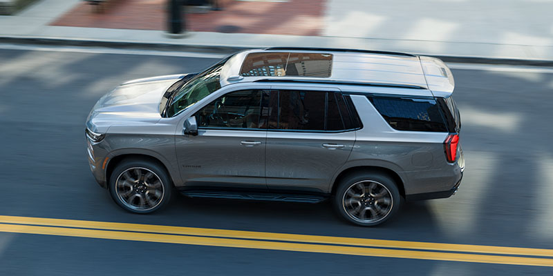 2026 Chevrolet Tahoe driving down a street in Mesa, AZ, showcasing its sleek design and modern features.