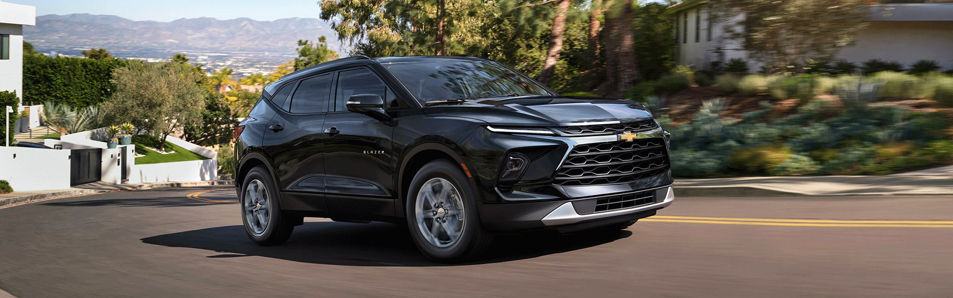 2026 Chevrolet Blazer in black driving on a curved road with greenery in the background.