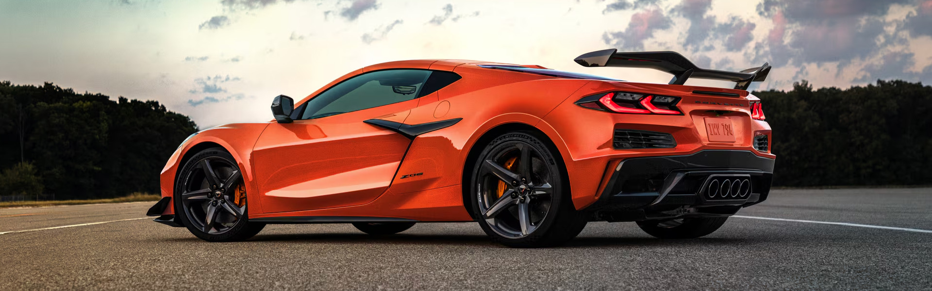 2026 Chevrolet Corvette Z06 in a vibrant orange color, parked on asphalt with a scenic background.
