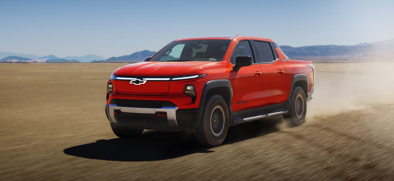 2026 Chevrolet Silverado EV electric pickup truck driving across a desert landscape with dust trailing behind.