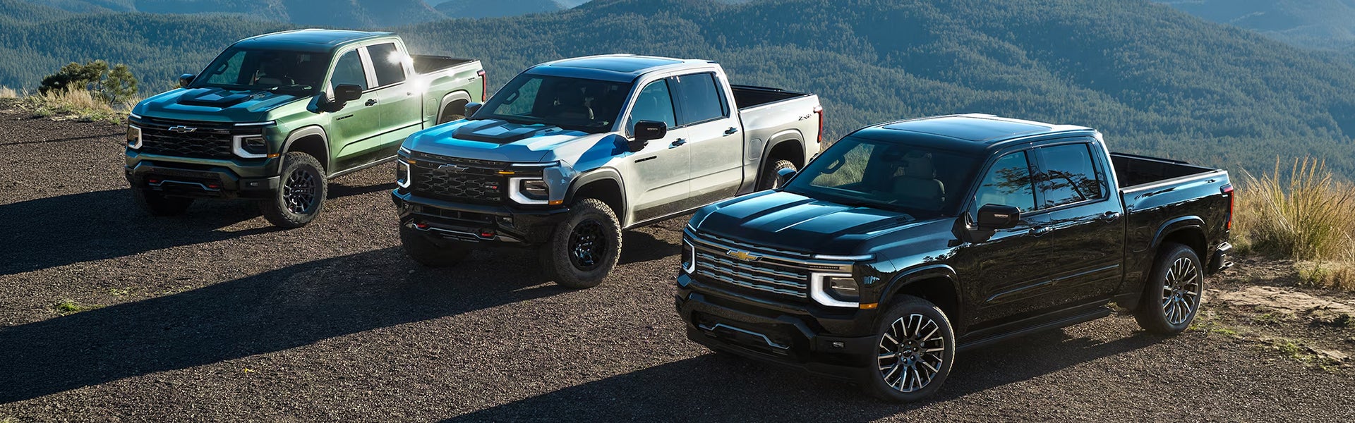 Three 2027 Chevrolet Silverado 1500 parked near mountain landscape.
